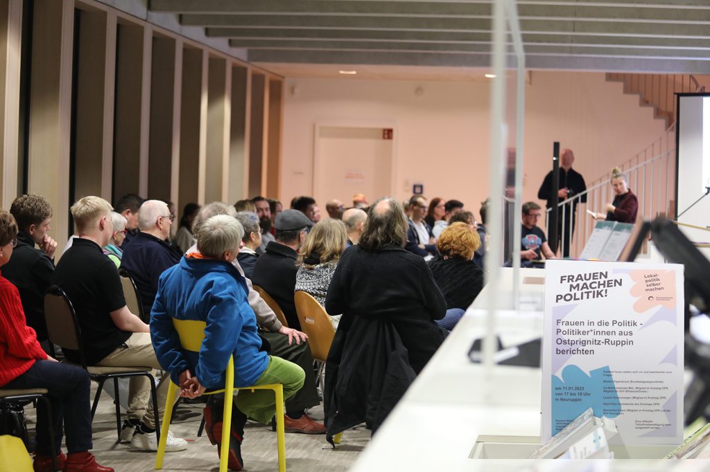 In dem Foyer des Museums Neuruppin sitzen die Besucher*innen der Veranstaltung. Der Raum ist gut gefüllt