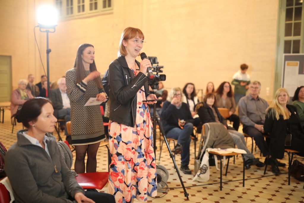 Eine Frau steht im Publikum, hält ein Mikrofon in der Hand und stellt den Podiumsteilnehmerinnen eine Frage